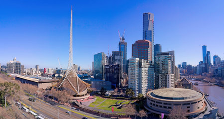 A sunny panoramic view of the Melbourne Arts Precinct, featuring the iconic white spire, the round concert hall, and the modern Southbank city skyline along the river.の写真素材