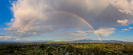 An aerial landscape shot of Melbourne's outer eastern suburbs featuring luxury homes and dense greenery, framed by a vibrant rainbow after a storm.の写真素材