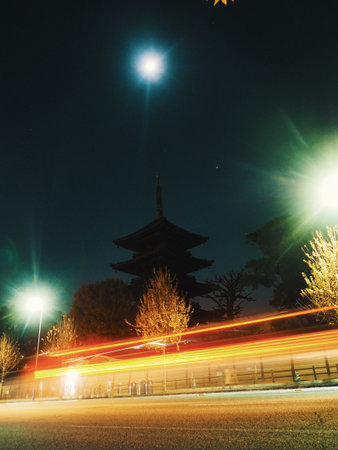 KYOTO, JAPAN - DECEMBER 3, 2022: The silhouette of the Toji Temple pagoda stands against the night sky in Kyoto. Below the ancient wooden tower, the motion of modern traffic creates vibrant streaks of light.のeditorial素材