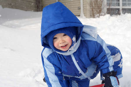 A toddler boy wearing a blue snowsuit playing in the snow.