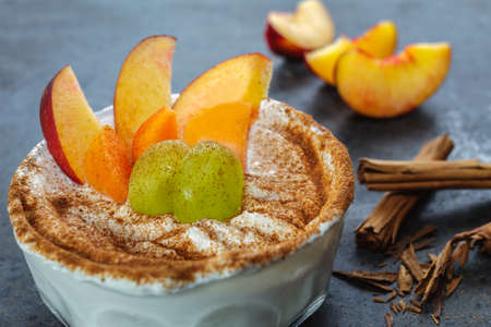 Glass bowl with Greek yogurt, fresh fruit and a sprinkle of cinnamon on a black marble background.の写真素材