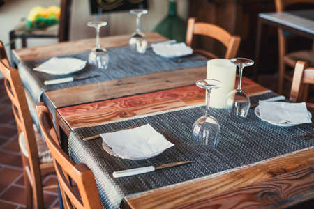 Light wooden table setting: white plates, rustic dark table cloth with salami, cheese, vine, and ham. Top view.の写真素材