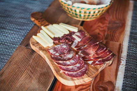 Light wooden table setting: white plates, rustic dark table cloth with salami, cheese, vine, and ham. Top view.の写真素材