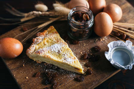 Traditional italian cake with ricotta cheese and raisin, eggs, jar and powdered sugar on wooden background, selective focusの写真素材