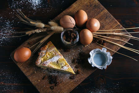 Traditional italian cake with ricotta cheese and raisin, eggs, jar and powdered sugar on wooden background, selective focusの写真素材