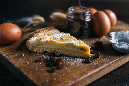 Traditional italian cake with ricotta cheese and raisin, eggs, jar and powdered sugar on wooden background, selective focusの写真素材