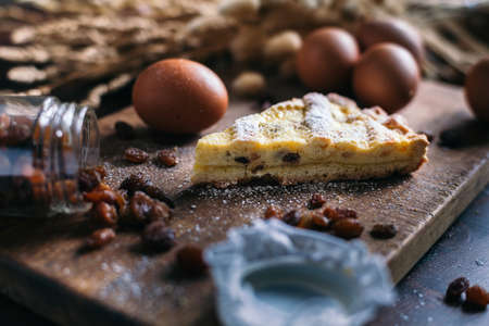 Traditional italian cake with ricotta cheese and raisin, eggs, jar and powdered sugar on wooden background, selective focusの写真素材