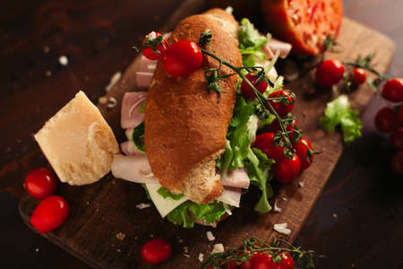 A view of a sandwich with a salad, cheese and ham on a wooden tableの写真素材