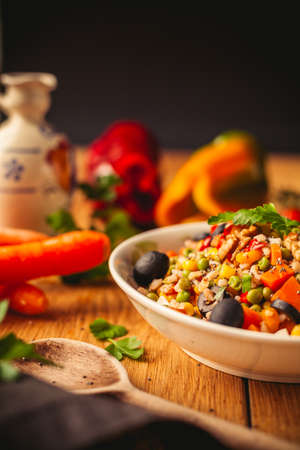 A view of a spelled dish on wooden background with some ingredients around: carrots, peppers, tomatos, parsley and oilの写真素材