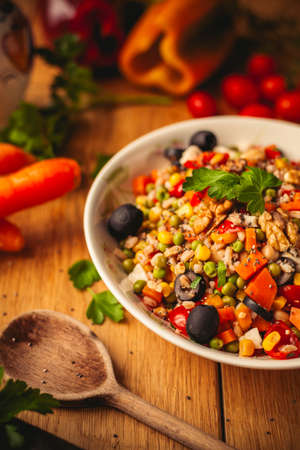 A view of a spelled dish on wooden background with some ingredients around: carrots, peppers, tomatos, parsley and oilの写真素材