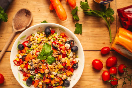 A view of a spelled dish on wooden background with some ingredients around: carrots, peppers, tomatos, parsley and oilの写真素材