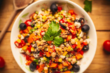 A view of a spelled dish on wooden background with some ingredients around: carrots, peppers, tomatos, parsley and oilの写真素材