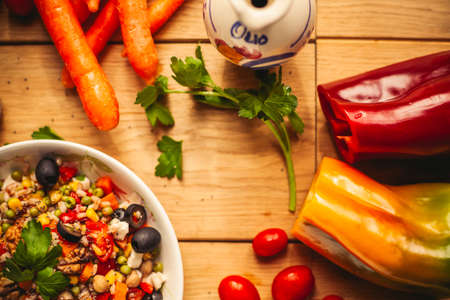 A view of a spelled dish on wooden background with some ingredients around: carrots, peppers, tomatos, parsley and oilの写真素材