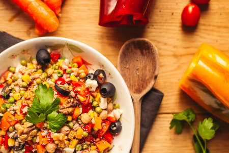 A view of a spelled dish on wooden background with some ingredients around: carrots, peppers, tomatos, parsley and oilの写真素材