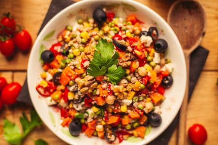 A view of a spelled dish on wooden background with some ingredients around: carrots, peppers, tomatos, parsley and oilの写真素材