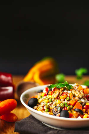 A view of a spelled dish on wooden background with some ingredients around: carrots, peppers, tomatos, parsley and oilの写真素材