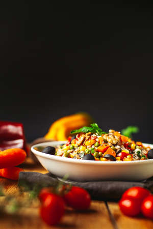 A view of a spelled dish on wooden background with some ingredients around: carrots, peppers, tomatos, parsley and oilの写真素材