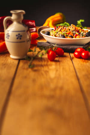 A view of a spelled dish on wooden background with some ingredients around: carrots, peppers, tomatos, parsley and oilの写真素材