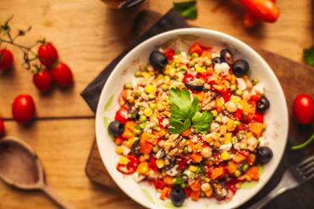 A view of a spelled dish on wooden background with some ingredients around: carrots, peppers, tomatos, parsley and oilの写真素材