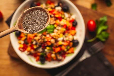 A view of a spelled dish on wooden background with some ingredients around: carrots, peppers, tomatos, parsley and oilの写真素材