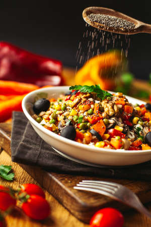 A view of a spelled dish on wooden background with some ingredients around: carrots, peppers, tomatos, parsley and oilの写真素材