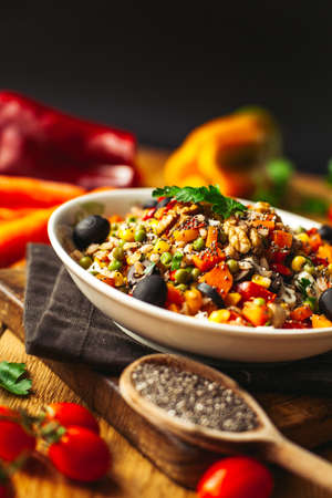 A view of a spelled dish on wooden background with some ingredients around: carrots, peppers, tomatos, parsley and oilの写真素材