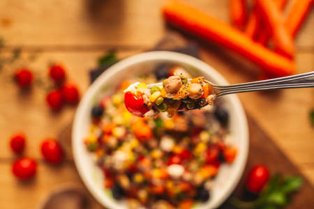 A view of a spelled dish on wooden background with some ingredients around: carrots, peppers, tomatos, parsley and oilの写真素材