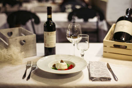 Light wooden table setting: white plates, rustic dark table cloth with mozzarella, cheese, vineの写真素材