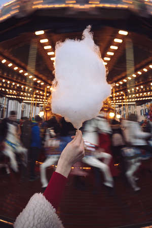Portrait of a beautiful young girl with white cotton candy in front of a carousel horse