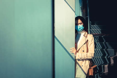 Girl with medical mask is staying inside a modern building during pandemic of Coronavirus Covid-19の写真素材