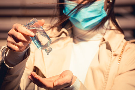 Girl with medical mask uses hand sanitizer gel to protect from Coronavirus Covid-19, outdoor cityの写真素材
