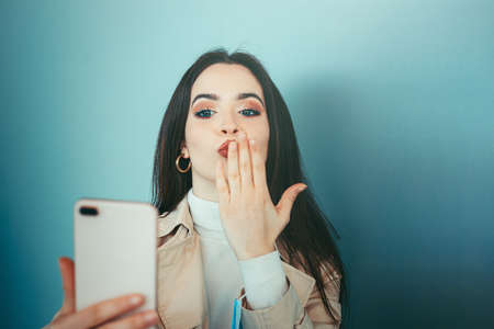 Cute girl is holding a medical mask in her hand and videocalling with smartphone during pandemic of Coronavirus Covid-19の写真素材