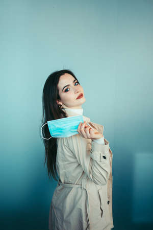 Cute girl is holding a medical mask in her hand and staying inside a modern building during pandemic of Coronavirus Covid-19の写真素材