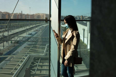 Girl with medical mask is using her smartphone in a modern building during pandemic of Coronavirus Covid-19の写真素材