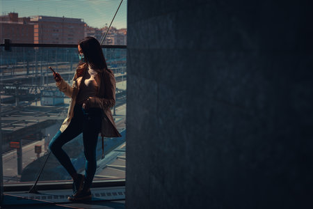 Girl with medical mask is using her smartphone in a modern building during pandemic of Coronavirus Covid-19の写真素材