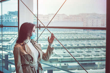 Girl in silohuette with medical mask is staying inside a modern building and look out of the window during pandemic of Coronavirus Covid-19の写真素材