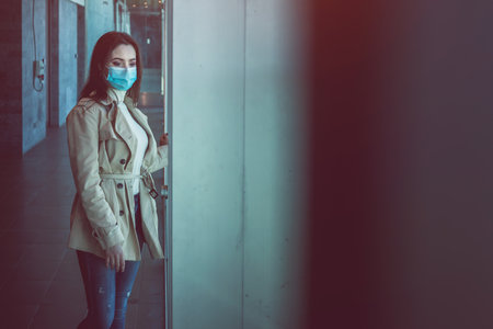 Girl with medical mask is staying inside a modern building during pandemic of Coronavirus Covid-19の写真素材