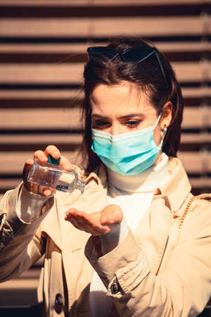 Girl with medical mask uses hand sanitizer gel to protect from Coronavirus Covid-19, outdoor cityの写真素材