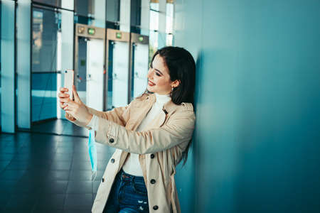 Cute girl is holding a medical mask in her hand and taking selfies with smartphone during pandemic of Coronavirus Covid-19の写真素材
