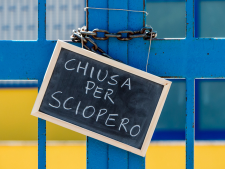 A closed gate school and a chalkboard hang on it. The gate is closed by a chain and the chalkboard is written, in italian words,の写真素材