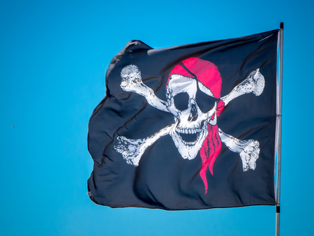 the pirates flag, the jolly roger, waving on a blue sky backgroundの写真素材