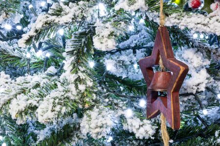 Close Up Of Christmas Snowy Tree With a Wooden Star and a Bell Decoration On Snowy Backgroundの写真素材