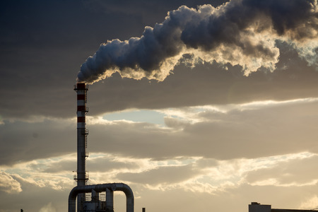 Smoking Red and White Bands Chimney On Backlight With White Smoke On Cloudy Sky Background At Sunset