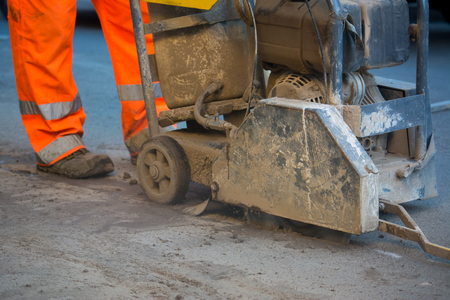 Close Up Of A Worker Dressing An Orange Uniform Driving A Machine To Cut The Asphalt In The Streetの写真素材