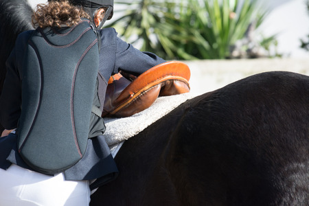 Backside Of Young Girl Preparing A Saddle Horse Before An Equestrian Competition On Blur Backgroundの写真素材