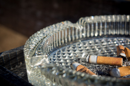 Close Up of A Glass Ashtray With Some Consumed Cigarettes On Blur Dark Backgroundの写真素材