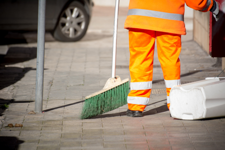 Horizontal View of a Dustman Cleaning the Street With a Mop Wearing an Orange Uniform in a Sunny Dayの写真素材
