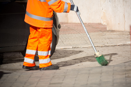 Horizontal View of a Dustman Cleaning the Street With a Mop Wearing an Orange Uniform in a Sunny Dayの写真素材
