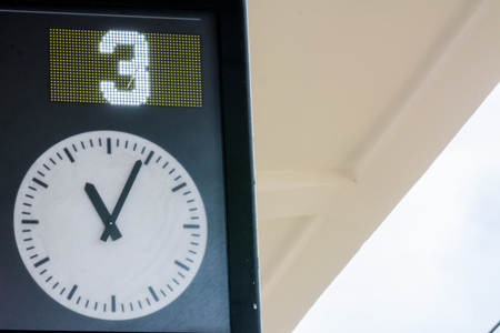 Horizontal View of Close Up of the Board Departures Indicating the Third Binary and a Clock at the Railway Station on Blur Cloudy Sky Background. Taranto, South of Italyの写真素材