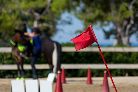Close Up of the Red Flag of Start on Blur Man Riding a Horse in a Riding School during a Competition...